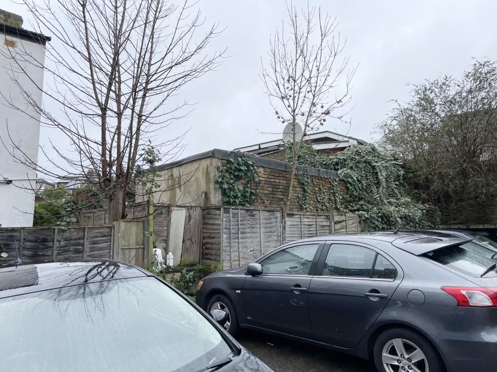 Lot: 149 - STAND-ALONE STORAGE BUILDING WITH POTENTIAL - Outside image of storage building from car parking area behind flats